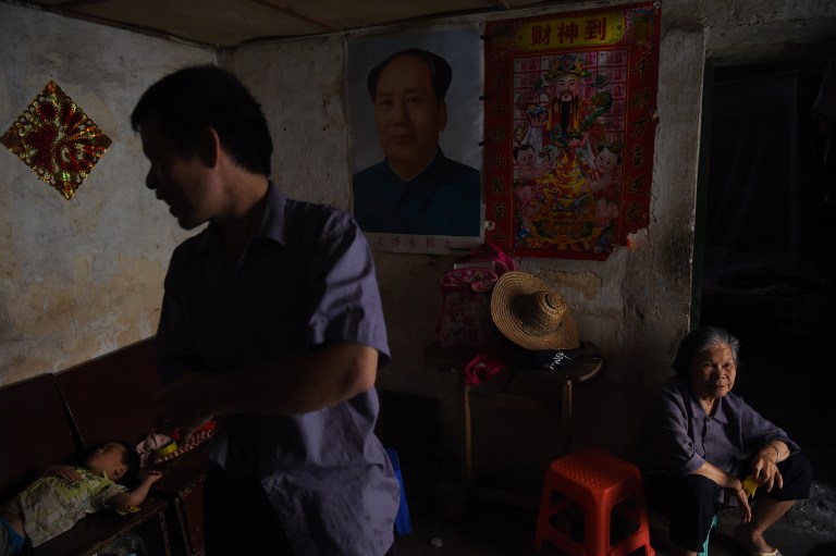 This photo taken on May 8, 2016 shows a family in their house with a portrait of late communist leader Mao Zedong in the old town of Wuxuan, in south China's Guangxi province. Launched by Mao in 1966 to topple his political enemies after the failure of the Great Leap Forward, the Cultural Revolution saw a decade of violence and destruction nationwide as party-led class conflict devolved into social chaos. Some of the worst excesses happened in Wuxuan, in the far southern region of Guangxi, where the hearts, livers and genitals of victims were cut out and fed to revellers. / AFP PHOTO / GREG BAKER / TO GO WITH China-politics-Cultural-history-rights-censorship,FOCUS by Benjamin CARLSON